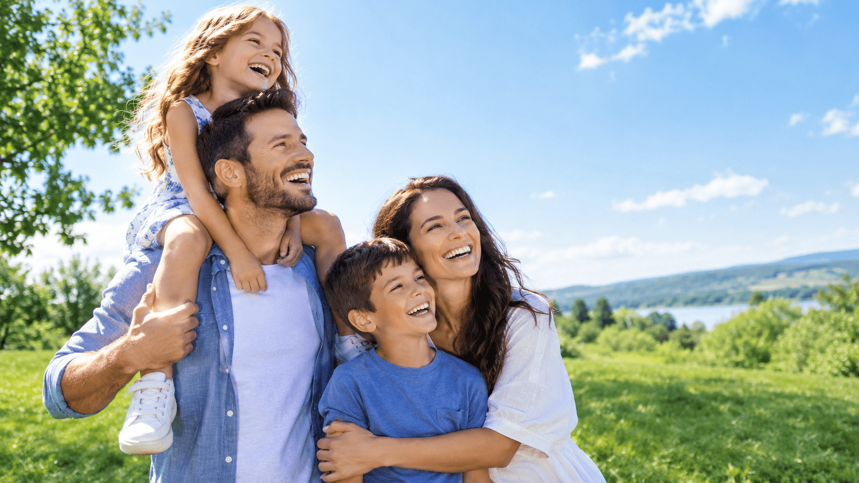 A laughing family in a green meadow under a clear blue sky